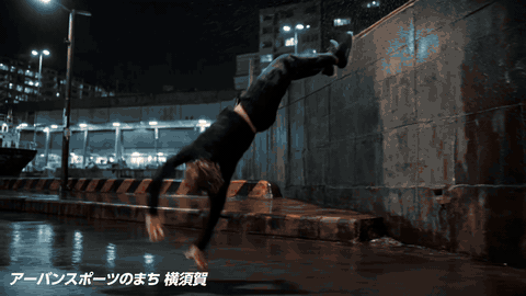 公式素材を使った参考カット。横須賀の街を背景にパルクール選手が動く制作イメージ。